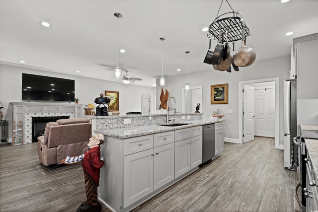 kitchen with sink, a center island with sink, a tile fireplace, pendant lighting, and stainless steel appliances