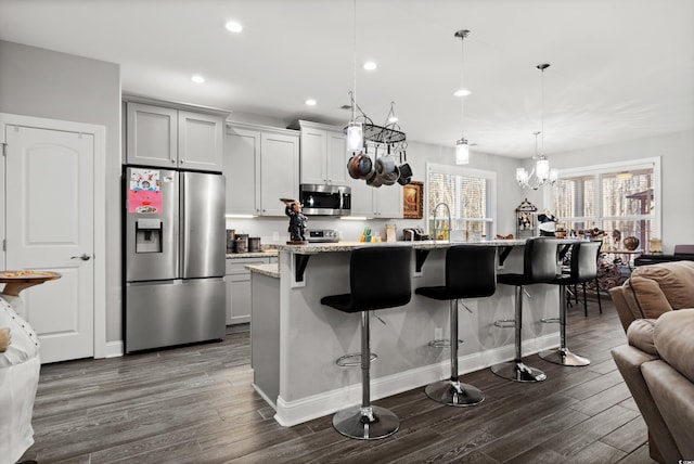 kitchen with appliances with stainless steel finishes, decorative light fixtures, an island with sink, a kitchen breakfast bar, and light stone counters