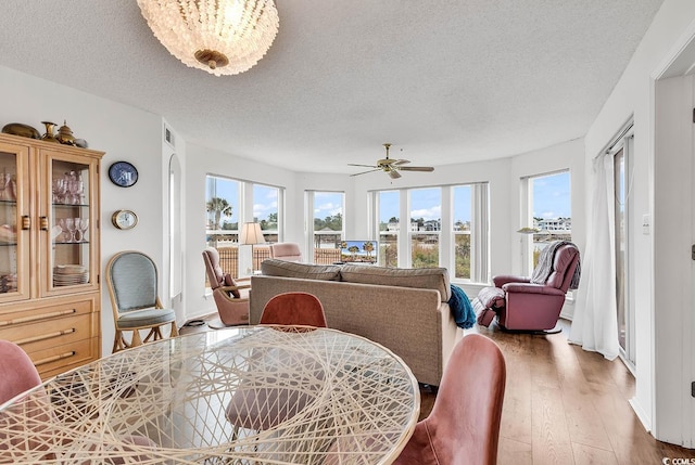 dining space with ceiling fan with notable chandelier, hardwood / wood-style floors, and a textured ceiling