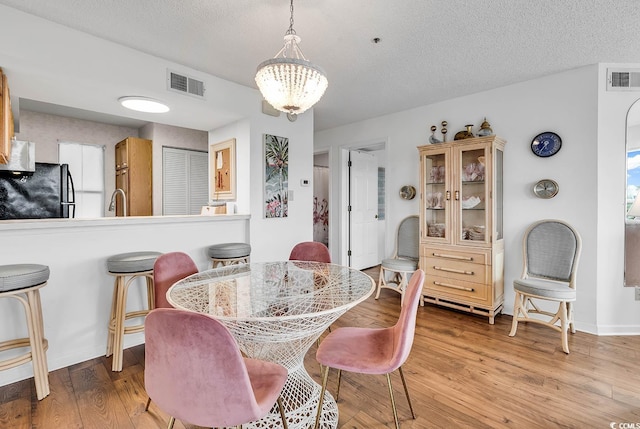 dining area featuring a notable chandelier, a textured ceiling, and light wood-type flooring