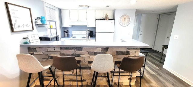 kitchen with a breakfast bar area, a peninsula, white appliances, white cabinetry, and light countertops