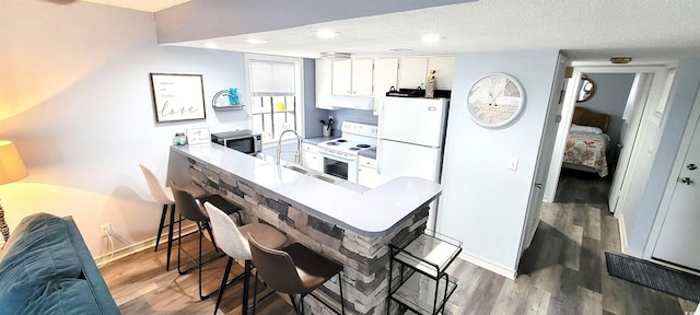 kitchen featuring white appliances, white cabinets, a kitchen breakfast bar, a peninsula, and light countertops