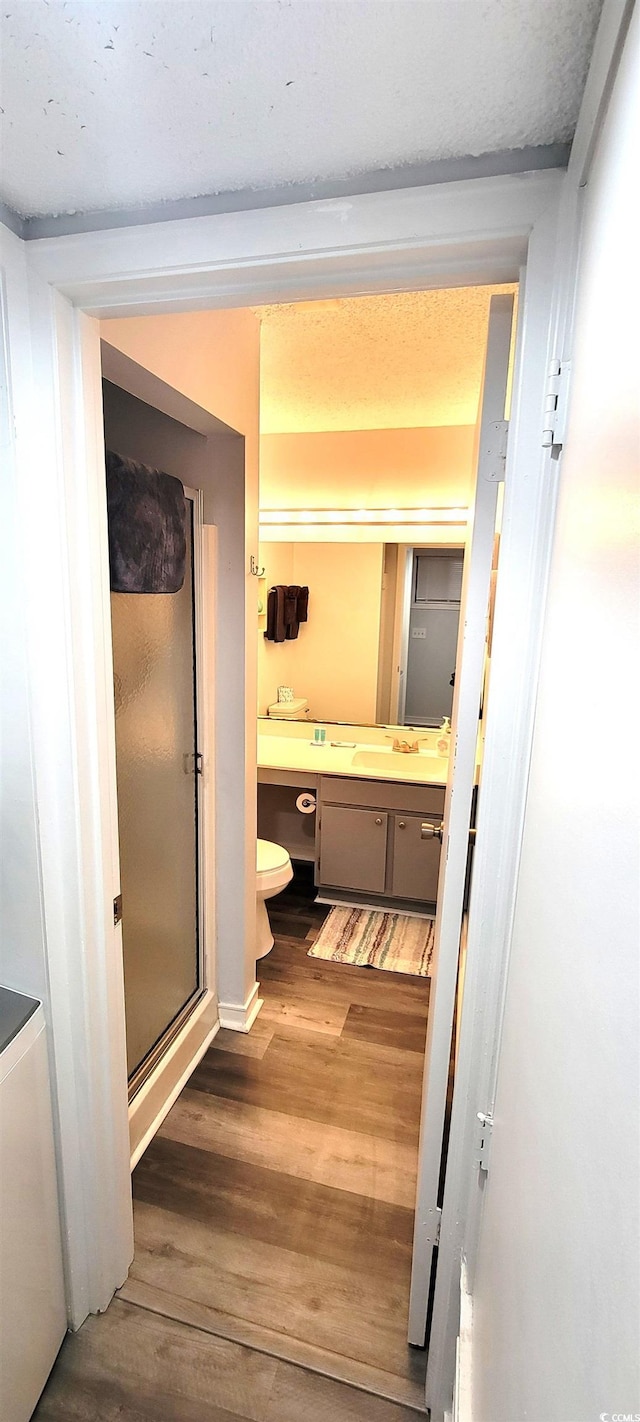 bathroom featuring toilet, a stall shower, wood finished floors, and vanity