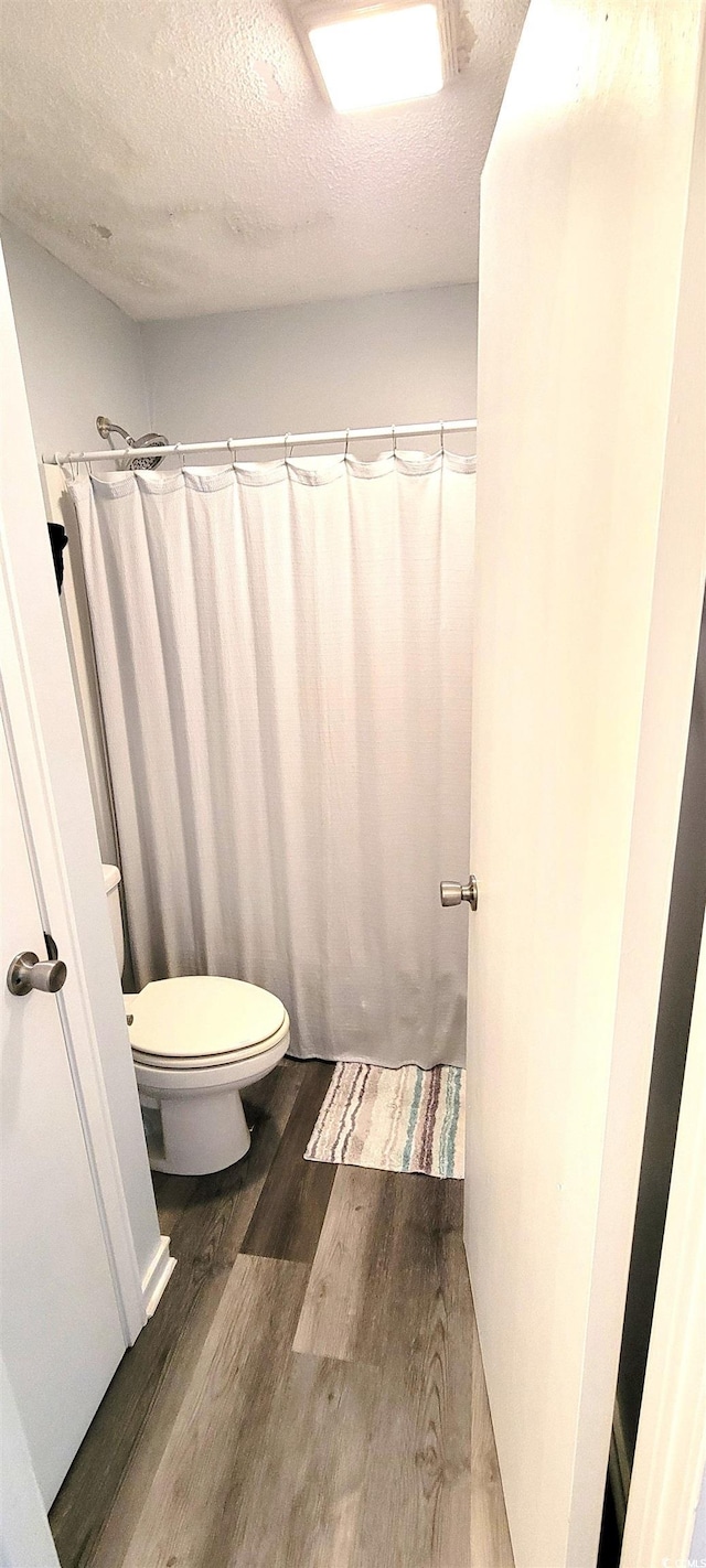 full bathroom featuring a textured ceiling, toilet, and wood finished floors