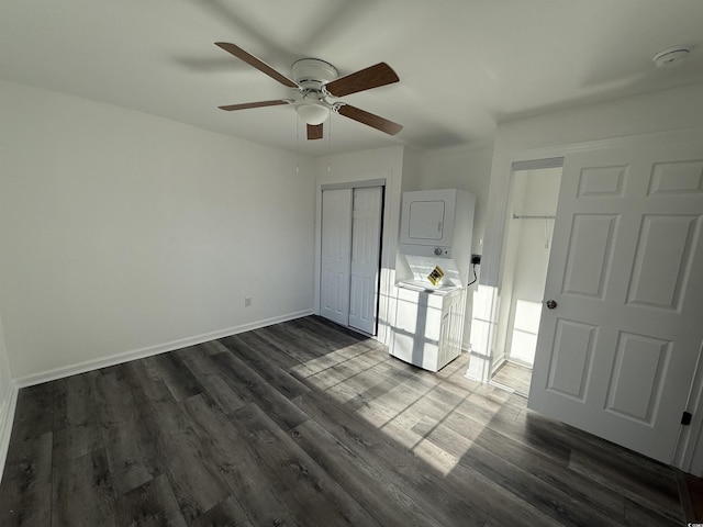 unfurnished bedroom with baseboards, stacked washer and clothes dryer, ceiling fan, dark wood-style flooring, and a closet