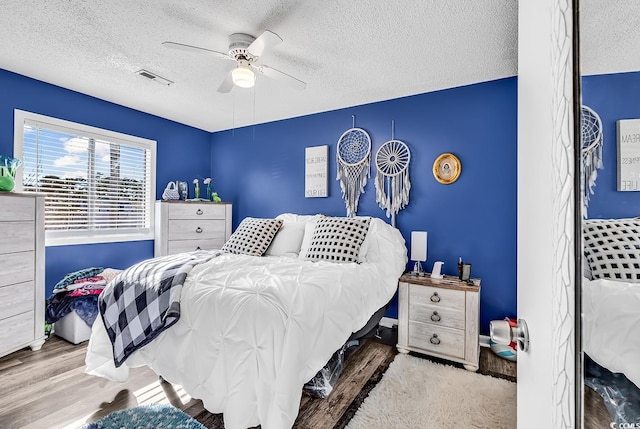 bedroom with ceiling fan, hardwood / wood-style floors, and a textured ceiling