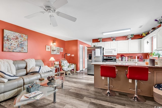 kitchen featuring appliances with stainless steel finishes, a kitchen bar, white cabinetry, ceiling fan, and light hardwood / wood-style flooring