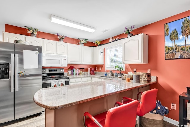 kitchen featuring white cabinets, appliances with stainless steel finishes, sink, and light stone counters