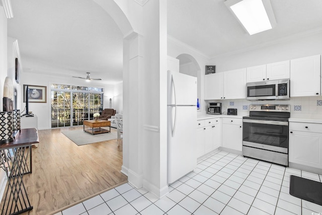 kitchen with stainless steel appliances, ornamental molding, white cabinets, and tasteful backsplash