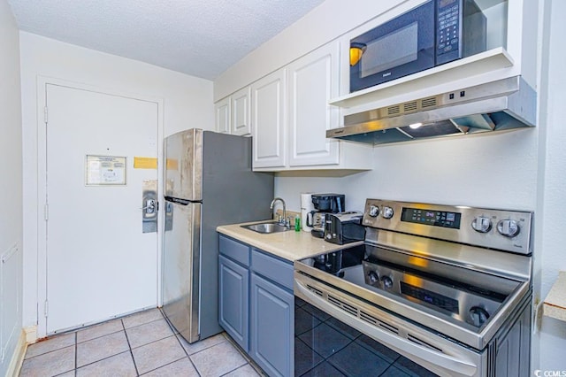 kitchen with light tile patterned floors, appliances with stainless steel finishes, a textured ceiling, white cabinets, and sink