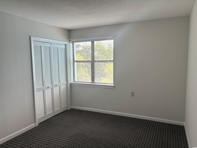 unfurnished bedroom featuring a textured ceiling, baseboards, dark colored carpet, and a closet