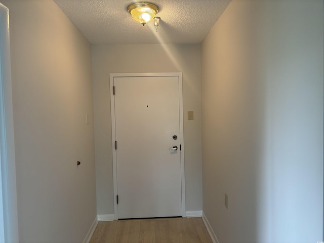 doorway to outside with light wood finished floors, baseboards, and a textured ceiling