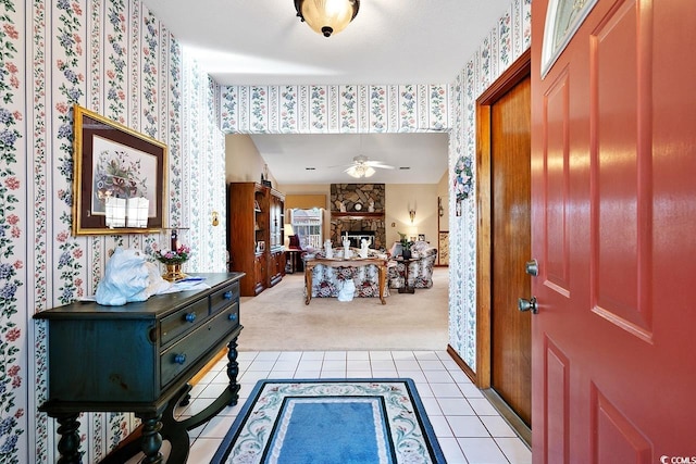 foyer with a fireplace, light tile patterned floors, light colored carpet, ceiling fan, and wallpapered walls