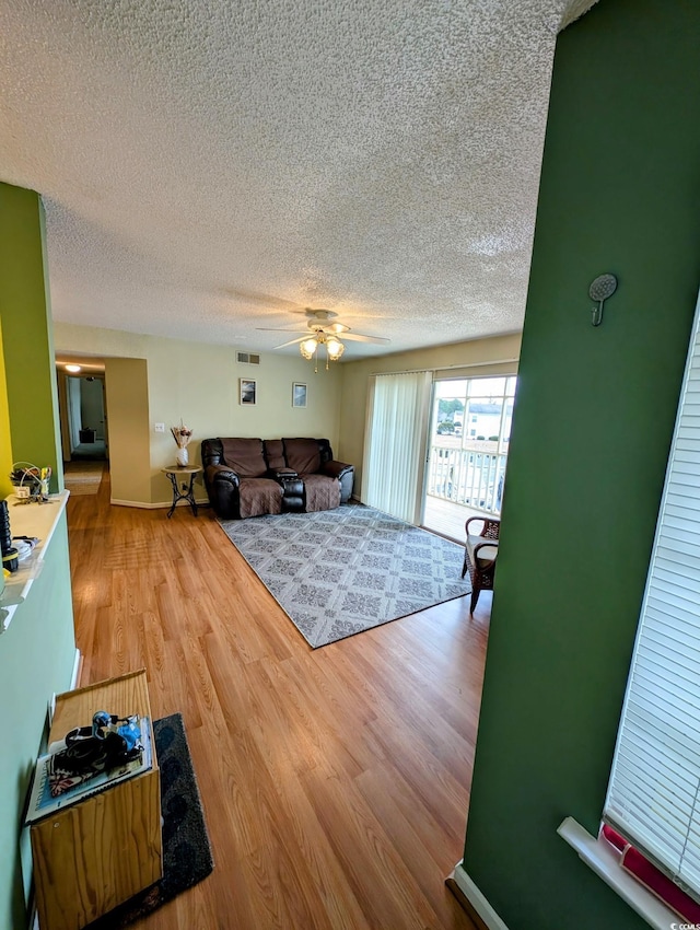 living room featuring ceiling fan, wood-type flooring, and a textured ceiling