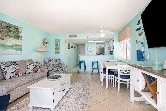 living area featuring light tile patterned floors, ceiling fan, visible vents, and a textured ceiling