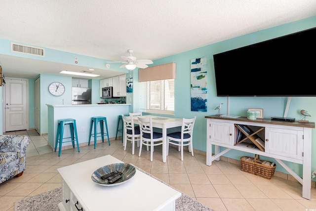 living area featuring light tile patterned floors, ceiling fan, a textured ceiling, visible vents, and baseboards