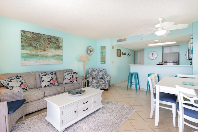 living area featuring light tile patterned floors, ceiling fan, visible vents, and a textured ceiling