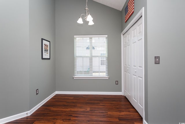 unfurnished dining area featuring dark wood-type flooring, a notable chandelier, baseboards, and vaulted ceiling