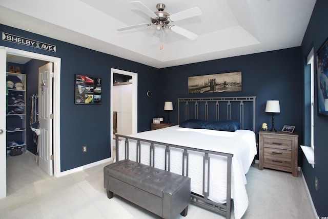 bedroom featuring a raised ceiling, baseboards, light colored carpet, ceiling fan, and a spacious closet