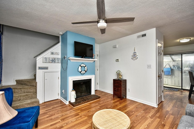 living room with ceiling fan, hardwood / wood-style floors, a textured ceiling, and a fireplace