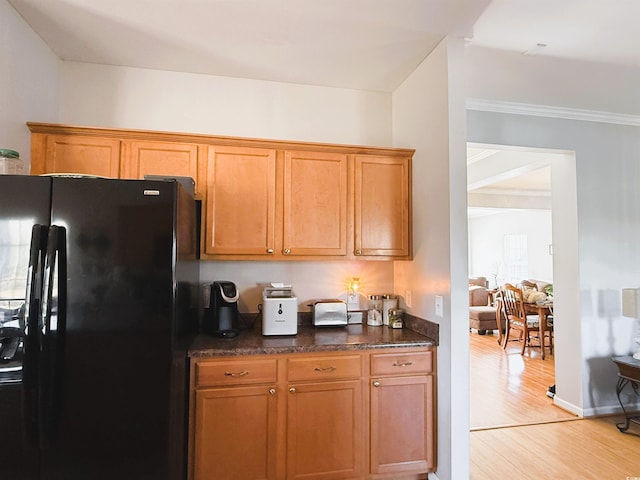 kitchen featuring dark stone counters, light wood-type flooring, freestanding refrigerator, and brown cabinets