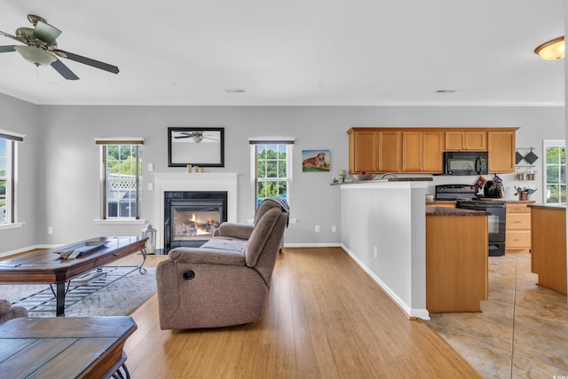 living area featuring a glass covered fireplace, ceiling fan, baseboards, crown molding, and light wood finished floors