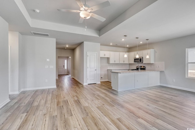 kitchen featuring light hardwood / wood-style floors, kitchen peninsula, a raised ceiling, decorative light fixtures, and white cabinets