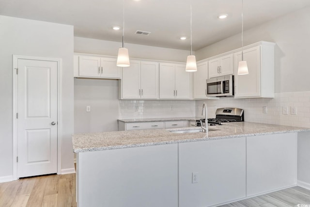 kitchen with kitchen peninsula, stainless steel appliances, white cabinets, and hanging light fixtures