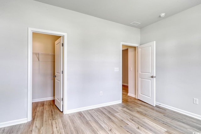 unfurnished bedroom featuring a closet, a spacious closet, and light hardwood / wood-style flooring