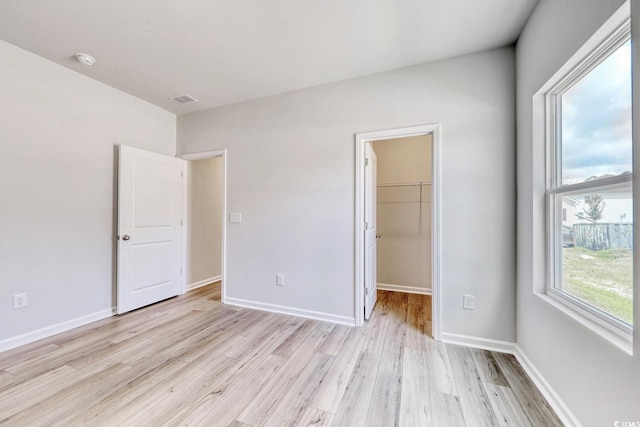 unfurnished bedroom featuring a spacious closet, a closet, and light wood-type flooring