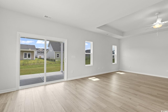 unfurnished room with ceiling fan, light hardwood / wood-style flooring, plenty of natural light, and a tray ceiling