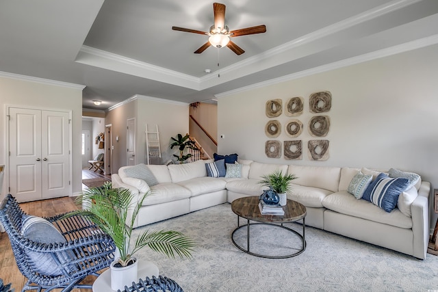 living room with ceiling fan, a tray ceiling, crown molding, and light wood-type flooring