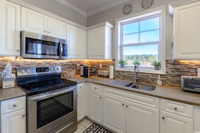 kitchen featuring light tile patterned flooring, a sink, ornamental molding, stainless steel appliances, and white cabinets