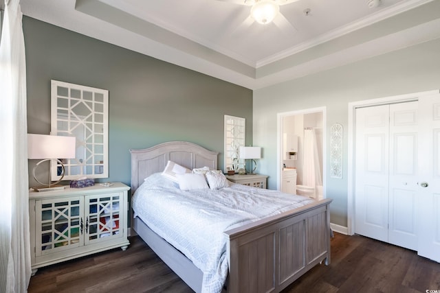 bedroom featuring a tray ceiling, a closet, ensuite bath, and dark wood-style flooring