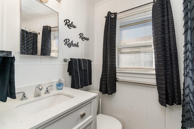 bathroom with toilet, vanity, wooden walls, and ornamental molding