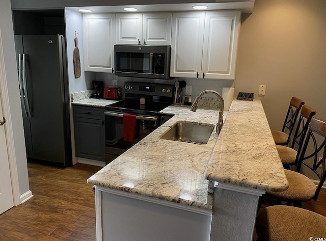 kitchen with white cabinetry, sink, a kitchen bar, kitchen peninsula, and stainless steel appliances