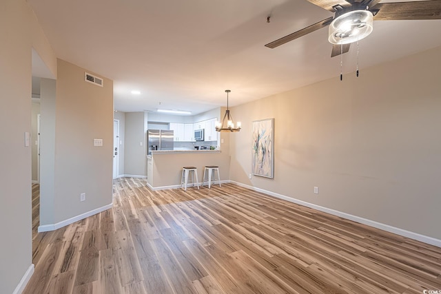 unfurnished living room featuring baseboards, ceiling fan with notable chandelier, visible vents, and light wood-style floors