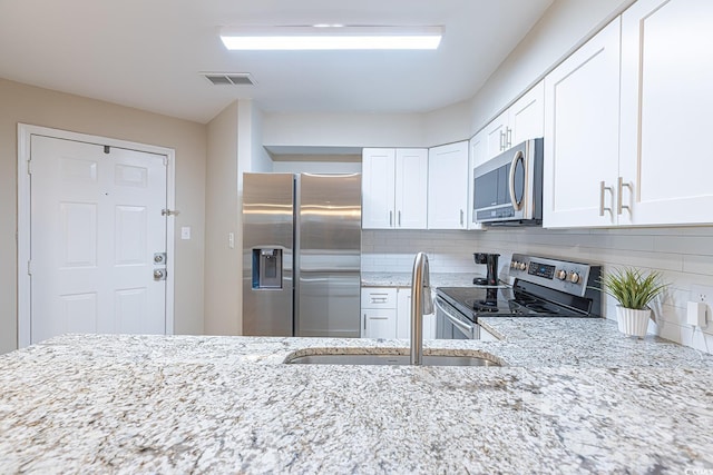 kitchen featuring light stone counters, stainless steel appliances, visible vents, white cabinetry, and a sink