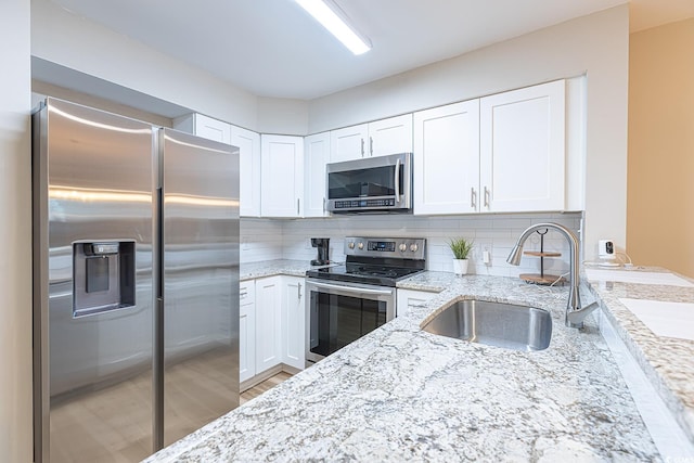 kitchen with appliances with stainless steel finishes, white cabinetry, sink, backsplash, and light stone counters