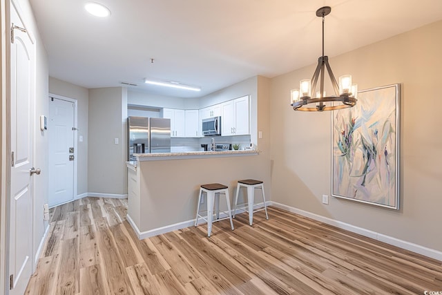 kitchen with baseboards, white cabinets, light wood-style flooring, appliances with stainless steel finishes, and a peninsula