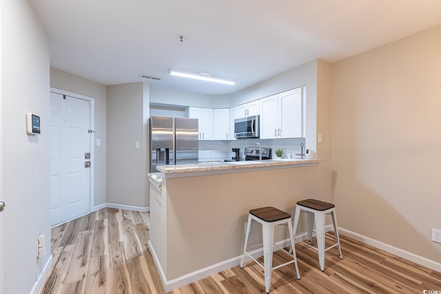 kitchen featuring a breakfast bar, stainless steel appliances, light wood finished floors, a peninsula, and white cabinetry