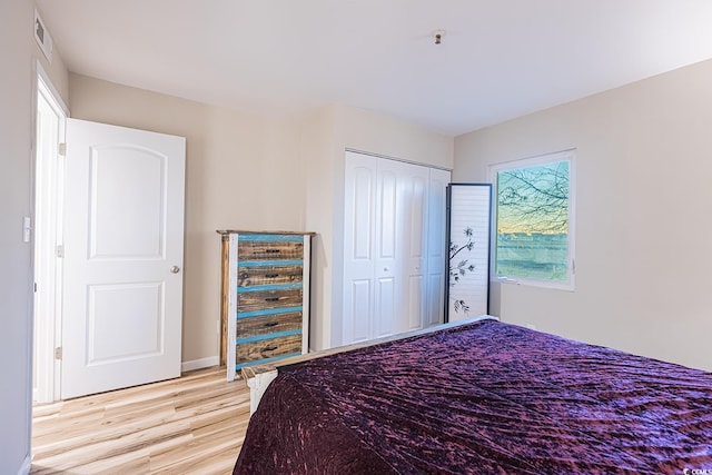 bedroom with baseboards, visible vents, light wood finished floors, and a closet