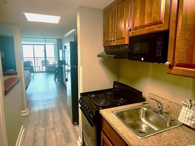 kitchen featuring black appliances, expansive windows, sink, and light hardwood / wood-style floors