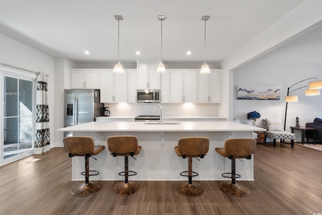 kitchen featuring a kitchen island with sink, a sink, hanging light fixtures, appliances with stainless steel finishes, and light countertops