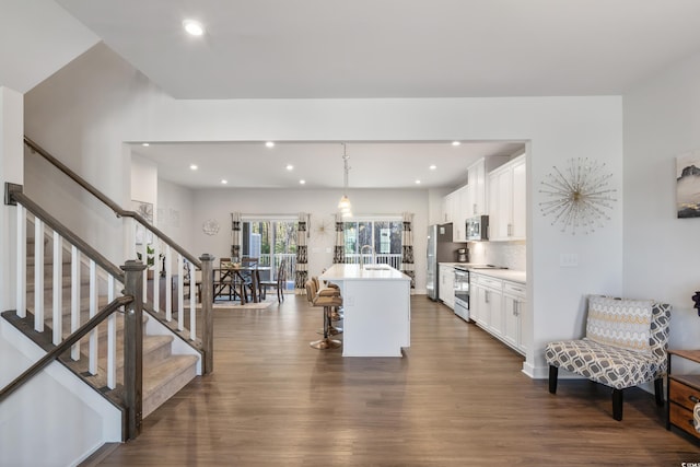 kitchen featuring a kitchen island with sink, stainless steel appliances, white cabinetry, light countertops, and hanging light fixtures