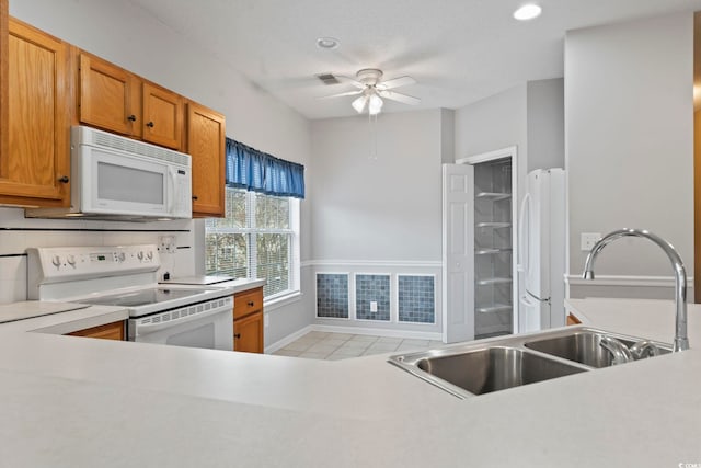 kitchen with light tile patterned flooring, white appliances, a sink, light countertops, and brown cabinetry