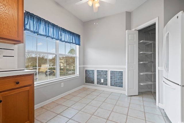 unfurnished dining area featuring ceiling fan, light tile patterned floors, and baseboards