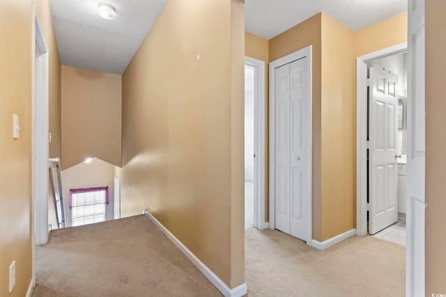 hall with a textured ceiling, baseboards, carpet flooring, and an upstairs landing