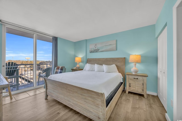 bedroom with access to exterior, a closet, floor to ceiling windows, and light hardwood / wood-style floors