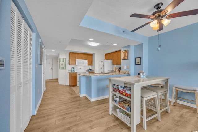 kitchen with light hardwood / wood-style floors, a kitchen bar, kitchen peninsula, white appliances, and sink